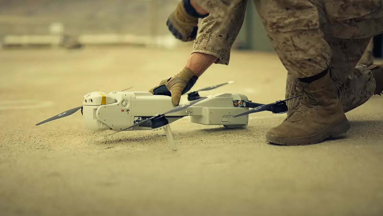 A soldier sets a white FLIR quadcopter drone down on desert ground